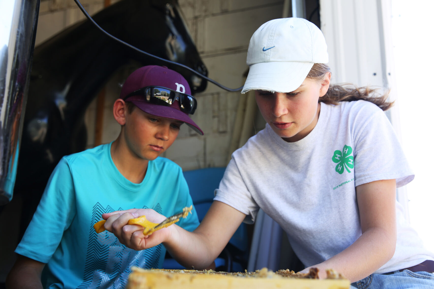 Elsa shows her brother Zack an easier way to use the uncapping fork to remove the honey